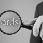 Man sucht mit Lupe das Wort Keywords - bildlich für Kanzleimarketing und Suchmaschinenoptimierung